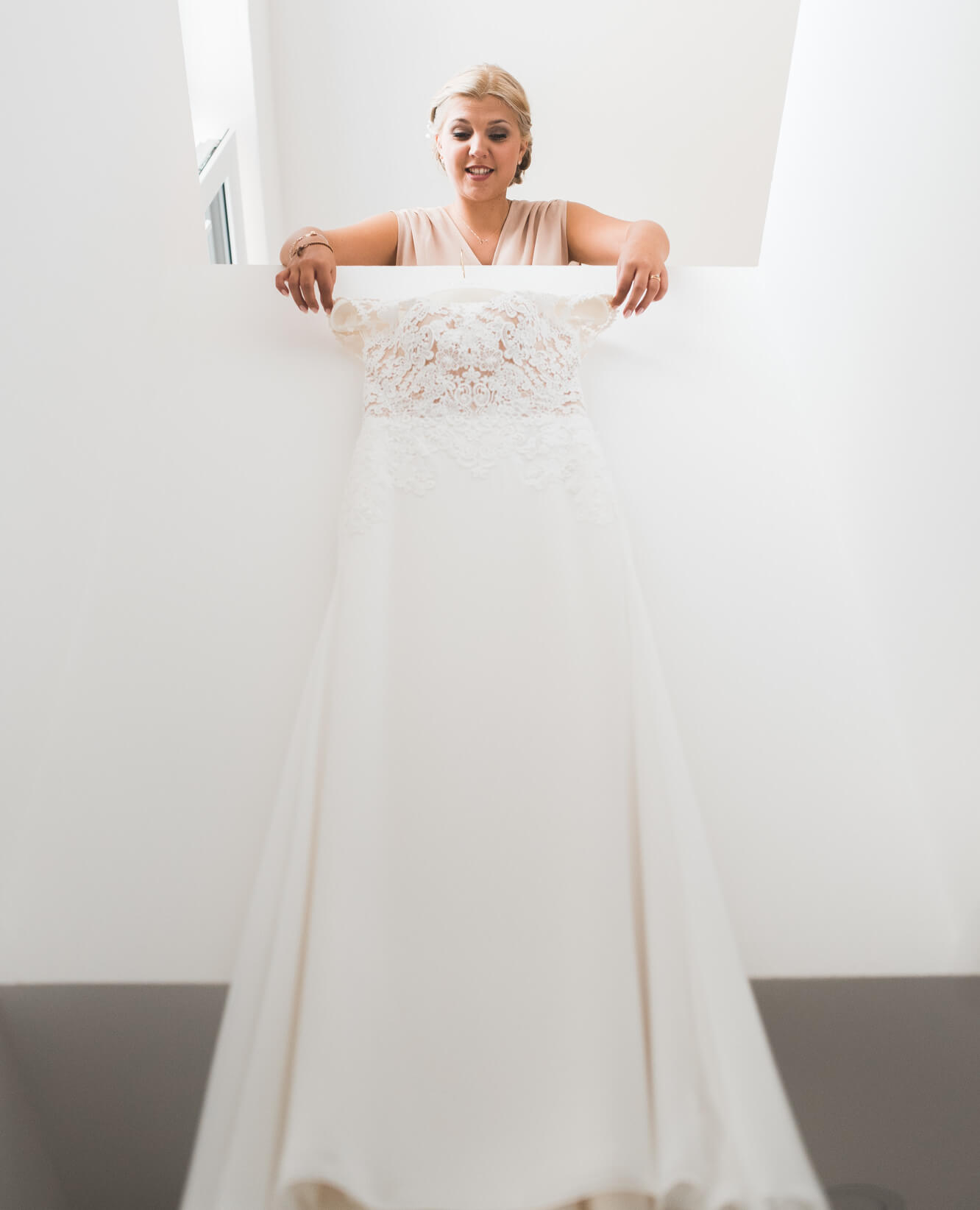 Braut hängt Hochzeitskleid von Rembo Styling in der Wohnung auf