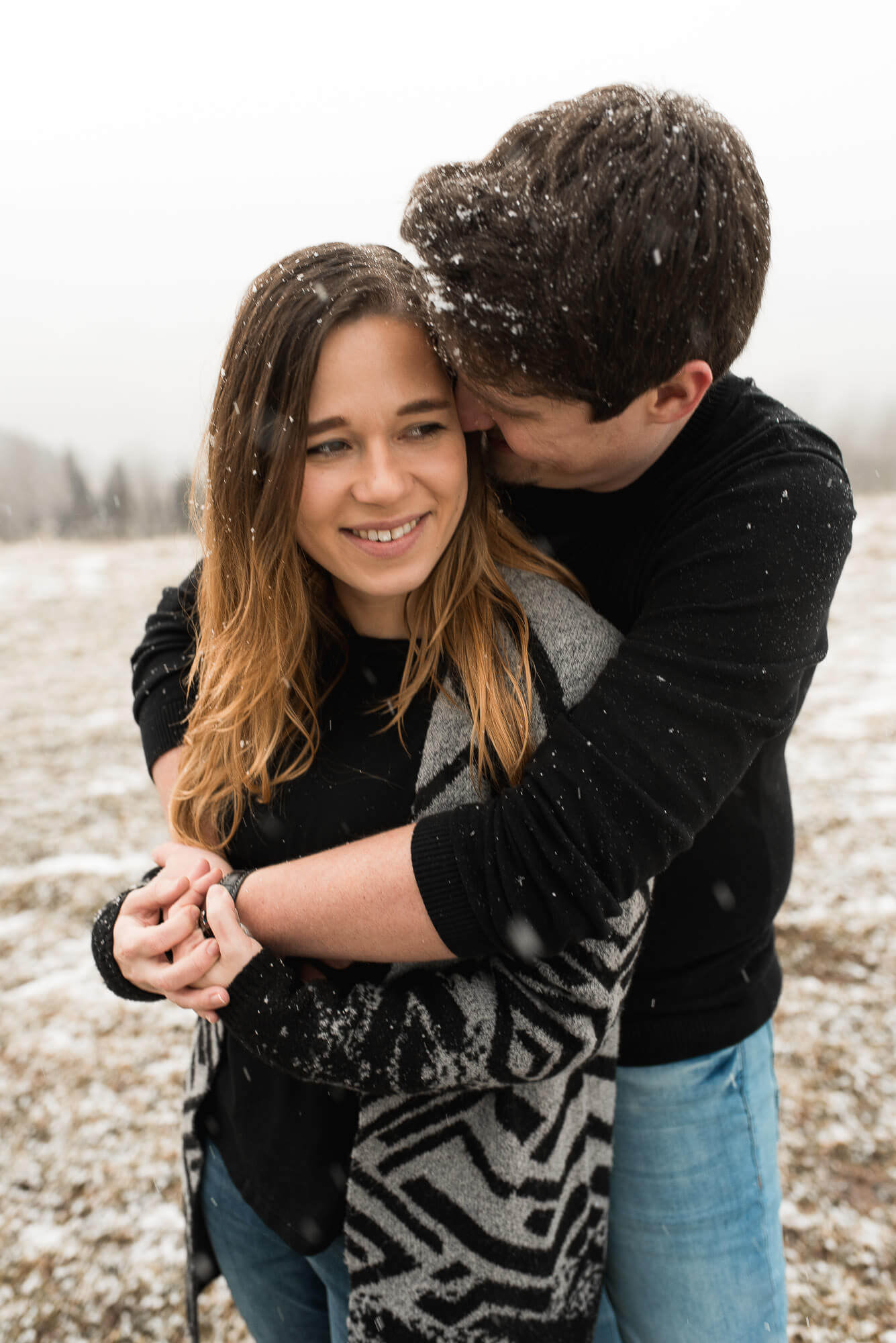 Er umarmt sie bei einem Verlobungsshooting im Winter bei Schnee