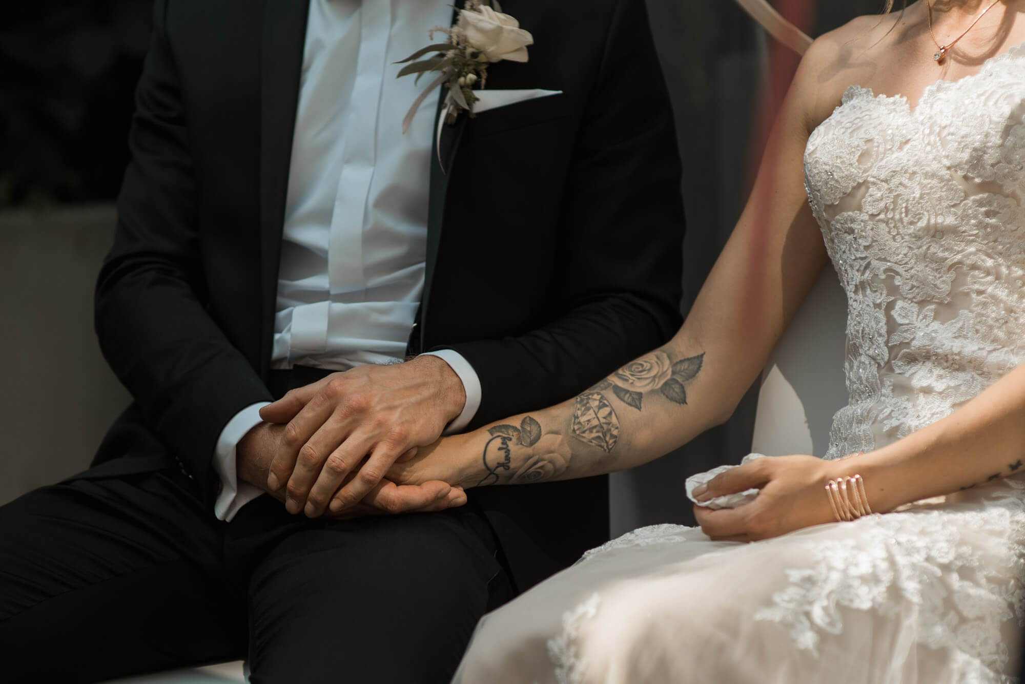 Bräutigam hält tattoowierte Hand der Braut während freier Trauung