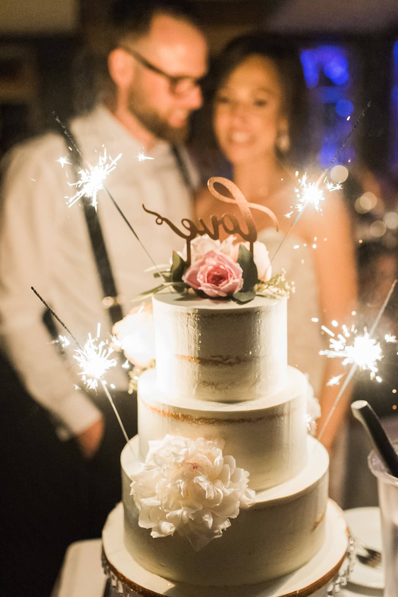 Naked Cake Hochzeitstorte von Naschwerk und Co mit Wunderkerzen mit Brautpaar bei Hochzeit im Hintergrund