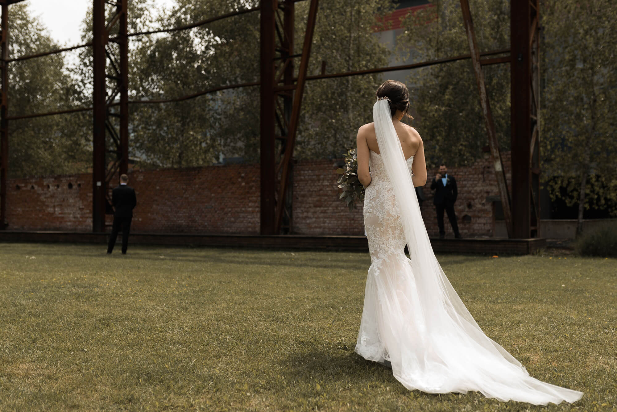 Braut mit Hochzeitskleid und Schleier läuft bei First Look auf den Bräutigam zu der mit dem Rücken zu ihr auf einer Wiese steht