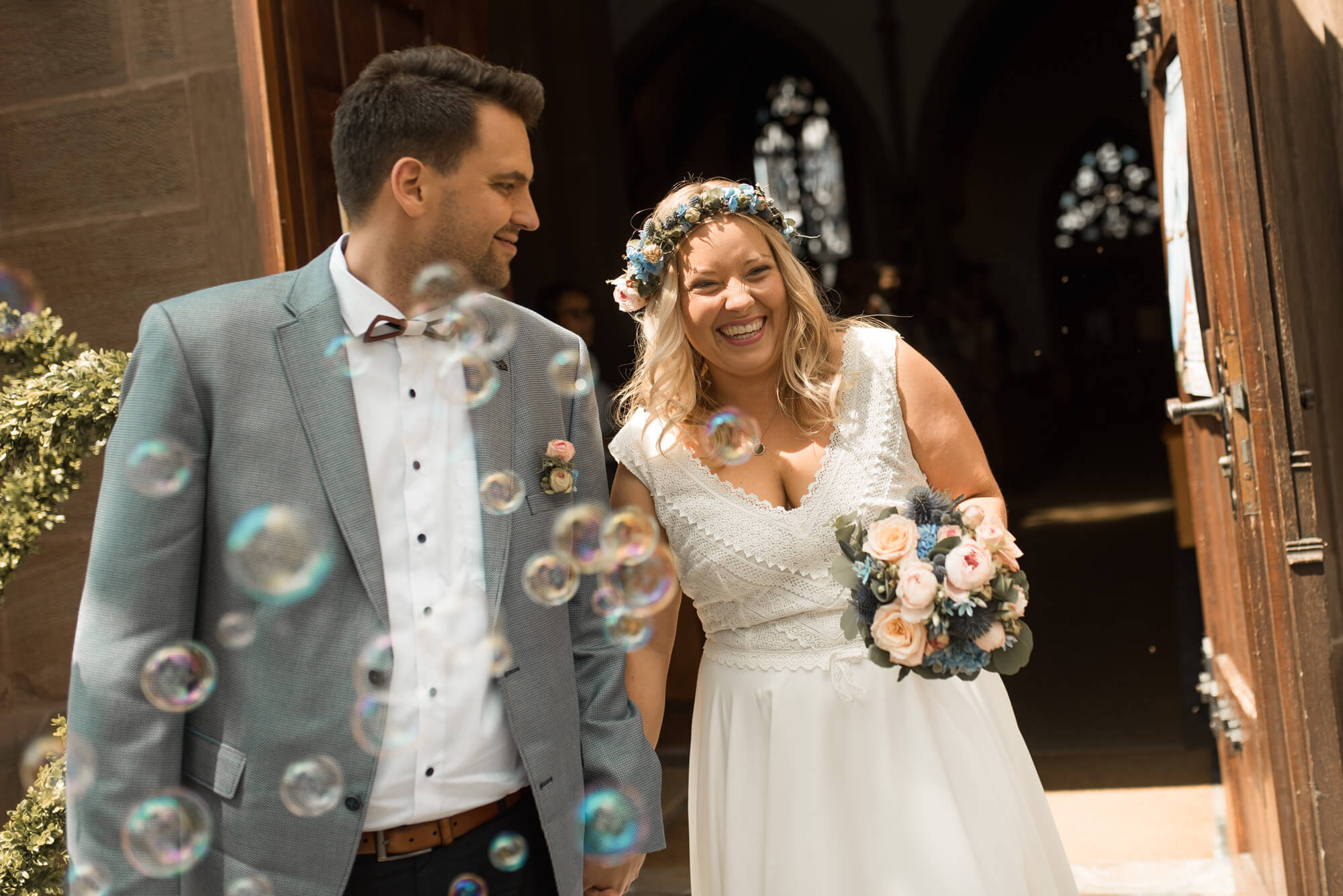 Brautpaar zieht nach Trauung aus Kirche aus lachend mit Seifenblasen Auszug