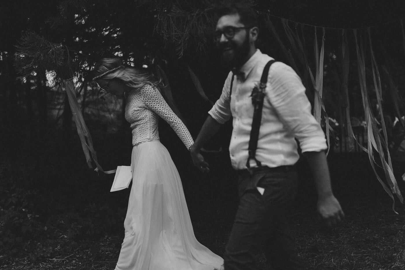 Brautpaar läuft Hand in Hand durch den Wald bei grüner Hochzeit in Schwarzweiss
