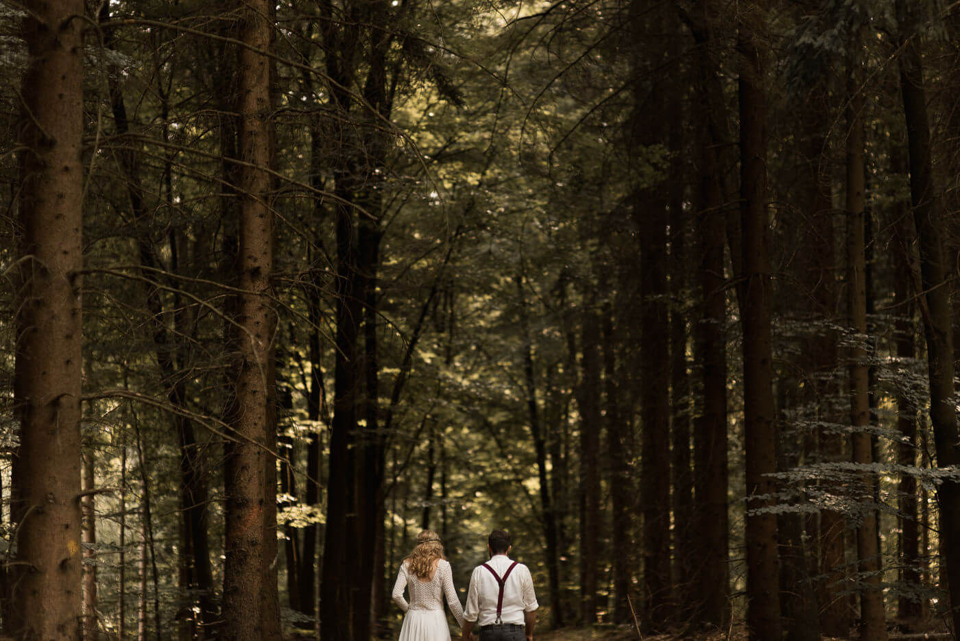 Brautpaar läuft mit Rücken zur Kamera in den Wald