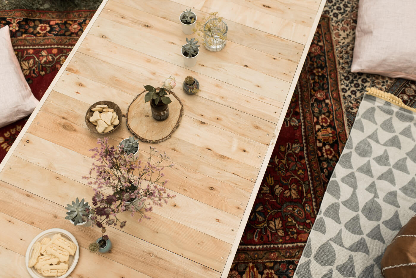 Holztisch mit Tischdekoration auf Teppich mit Sitzkissen auf Boho Hochzeit im Wald