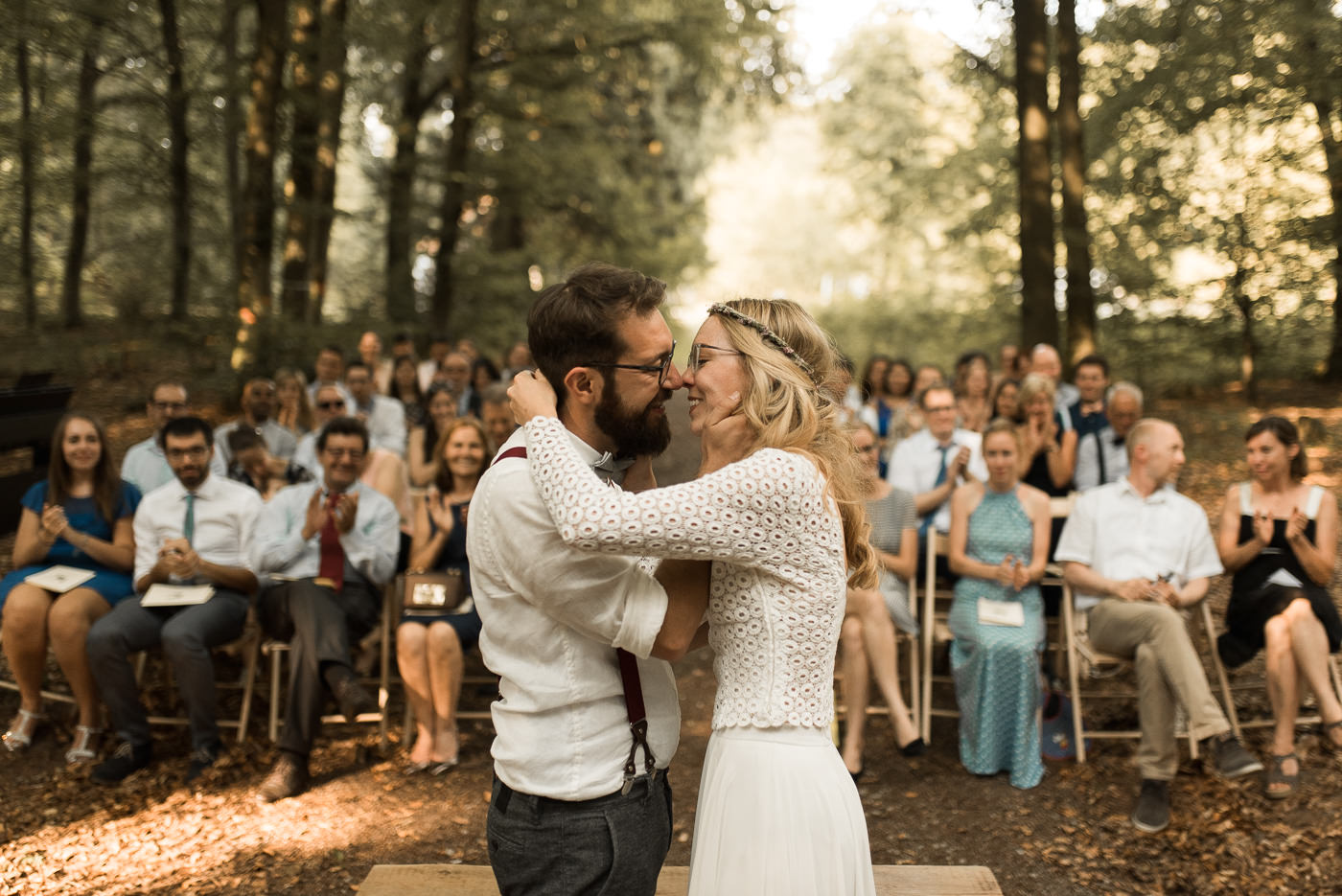 Brautpaar küsst sich bei Trauung vor Hochzeitsgesellschaft in Wald bei grüner Hochzeit und ist glücklich