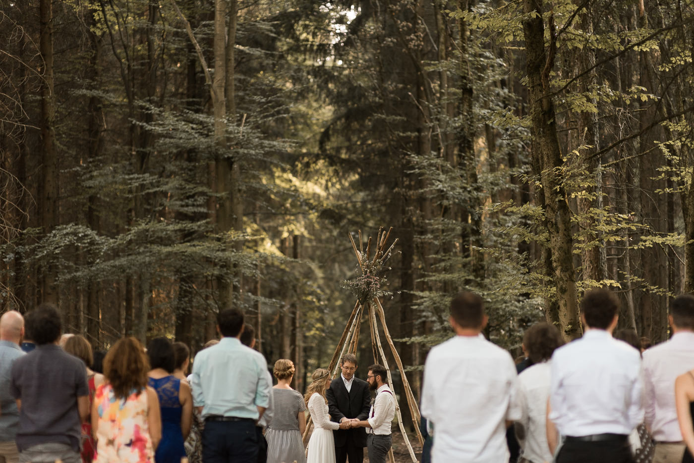 Trauung mit Eheversprechen und Trauredner in Wald unter Tipi zu Hochzeit im Grünen mit Hochzeitsgesellschaft auf Klappstühlen