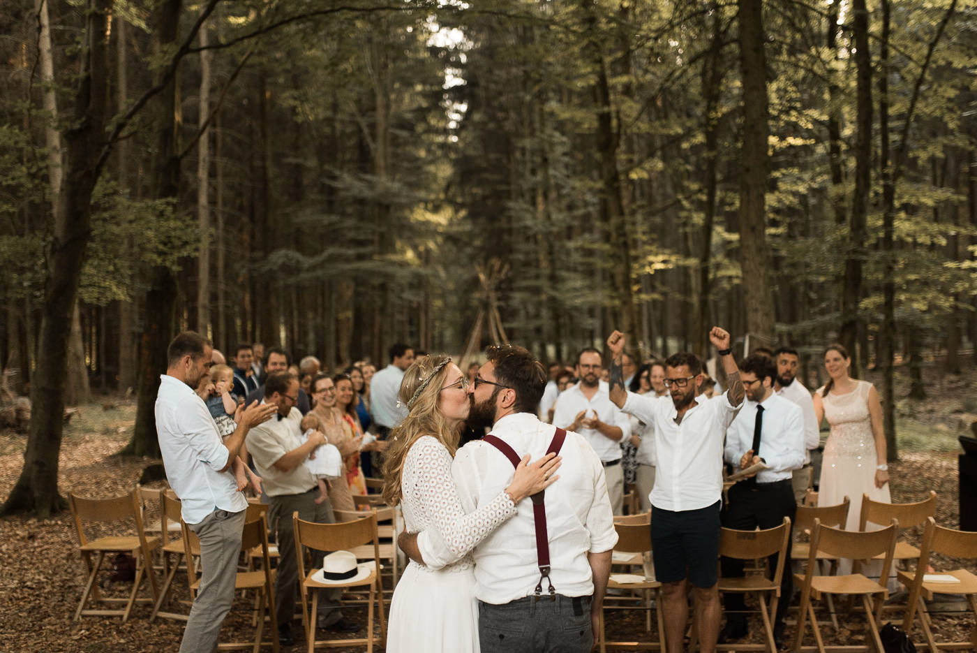 Wedding couple is kissing in front of the wedding guests after their green wedding ceremony in the forest