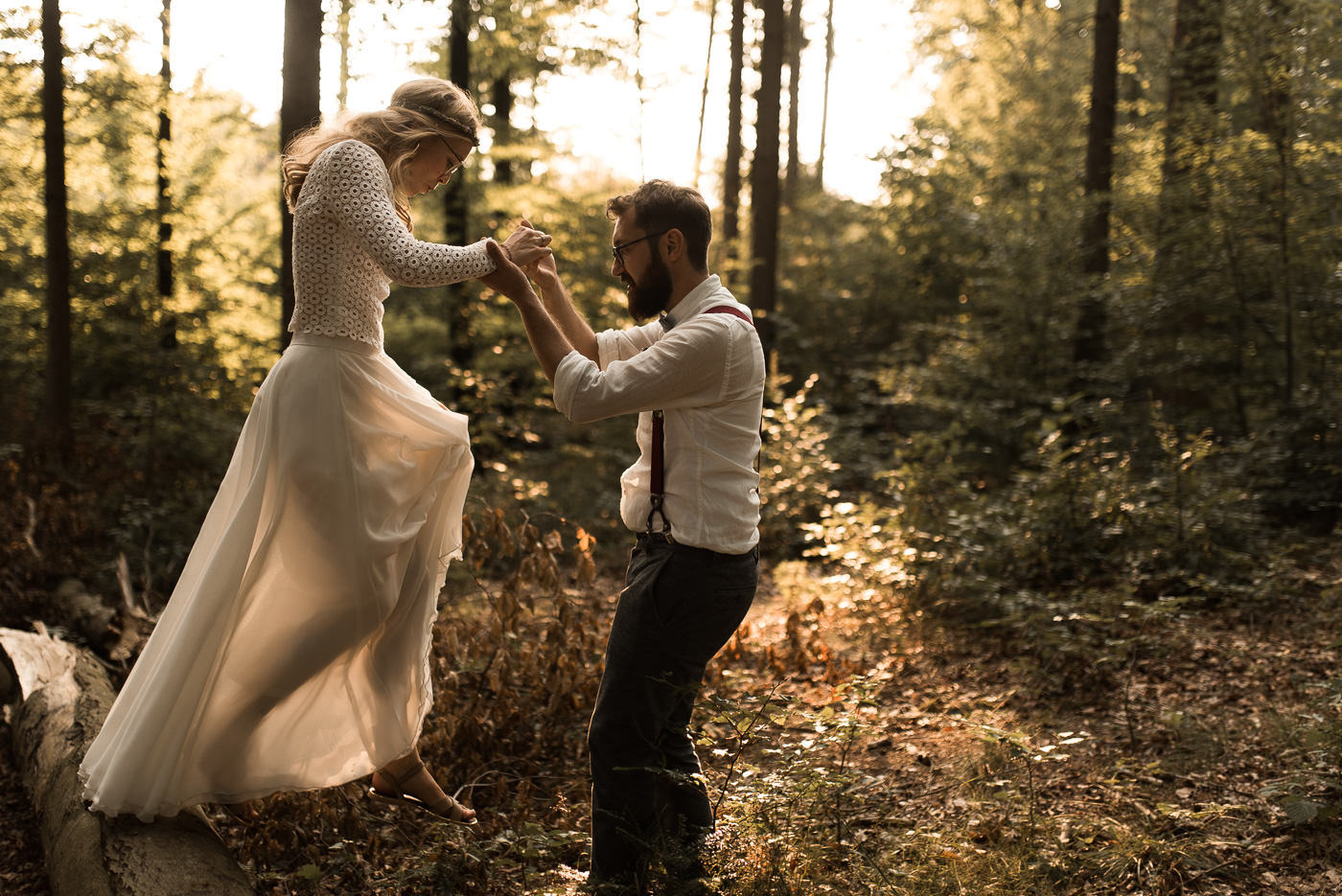 Braut springt von Baumstamm ihrem Bräutigam entgegen im Wald bei Waldhochzeit