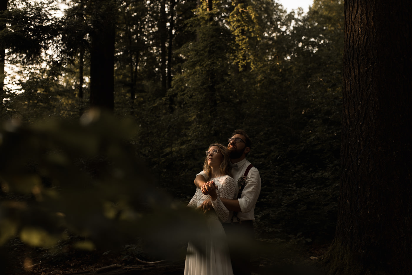 Groom holds his bride in his arms in a forest during the photoshoot of the bridal couple after their elopement