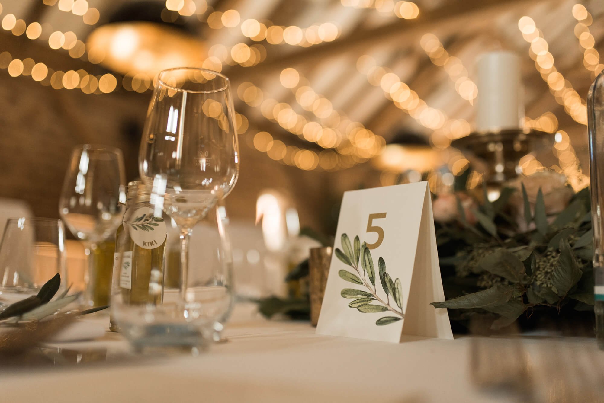 Tischdeko mit Tischkarte auf der Olivenblätter zu sehen sind mit Lichterketten im Hintergrund auf dem Landgut Lingental 