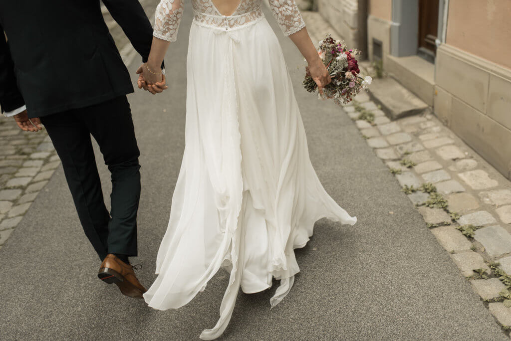 Brautpaar läuft Hand in Hand mit leicht fallendem Kleid