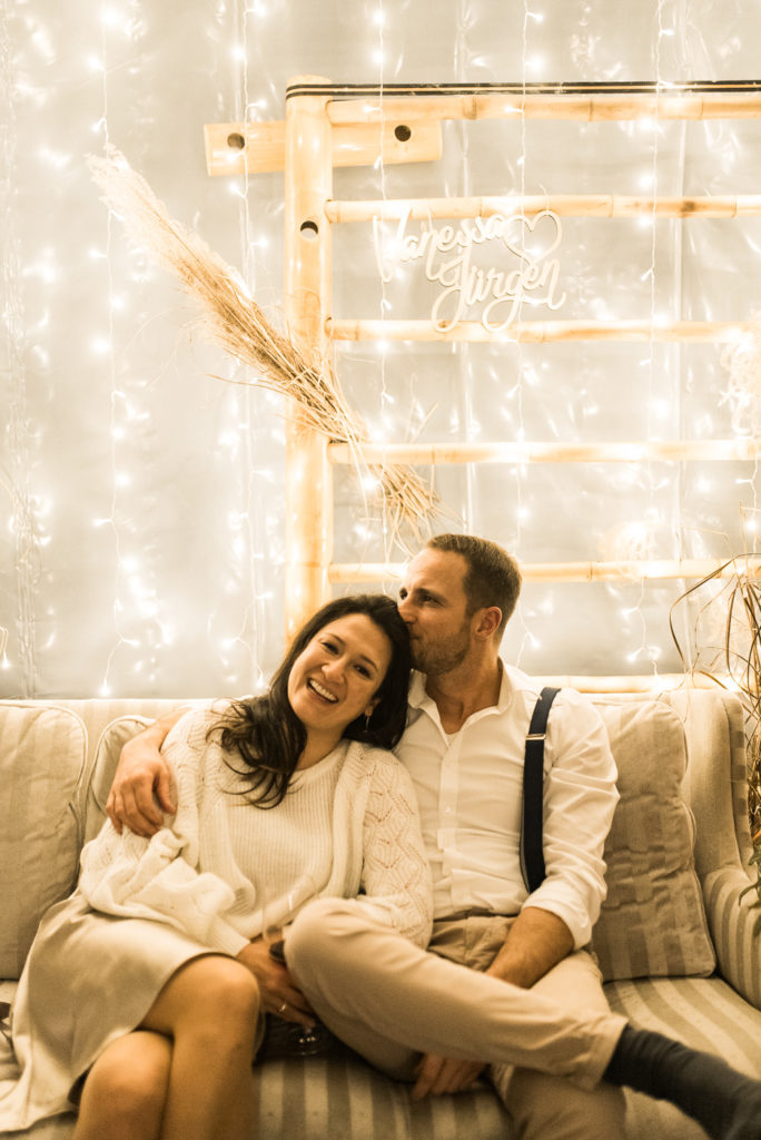 Brautpaar auf Sofa mit Lichterketten im Hintergrund und Pampasgras